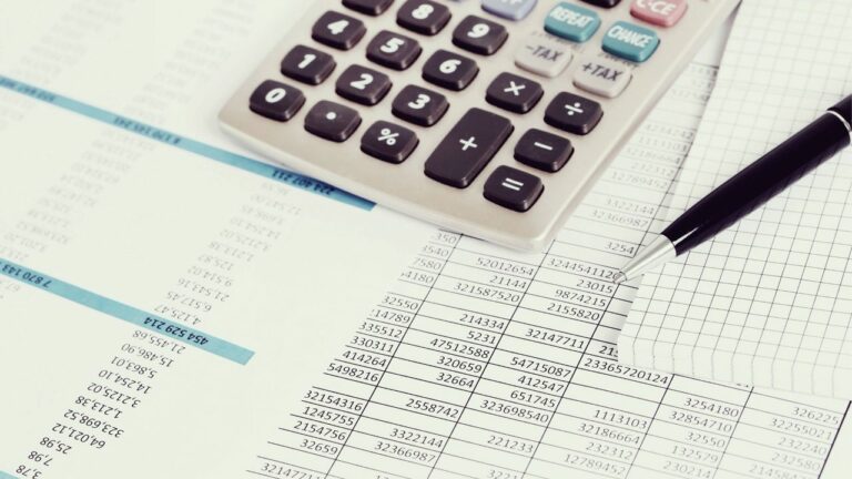 Calculadora e caneta sobre folhas com números, elementos relacionados à formação de preço