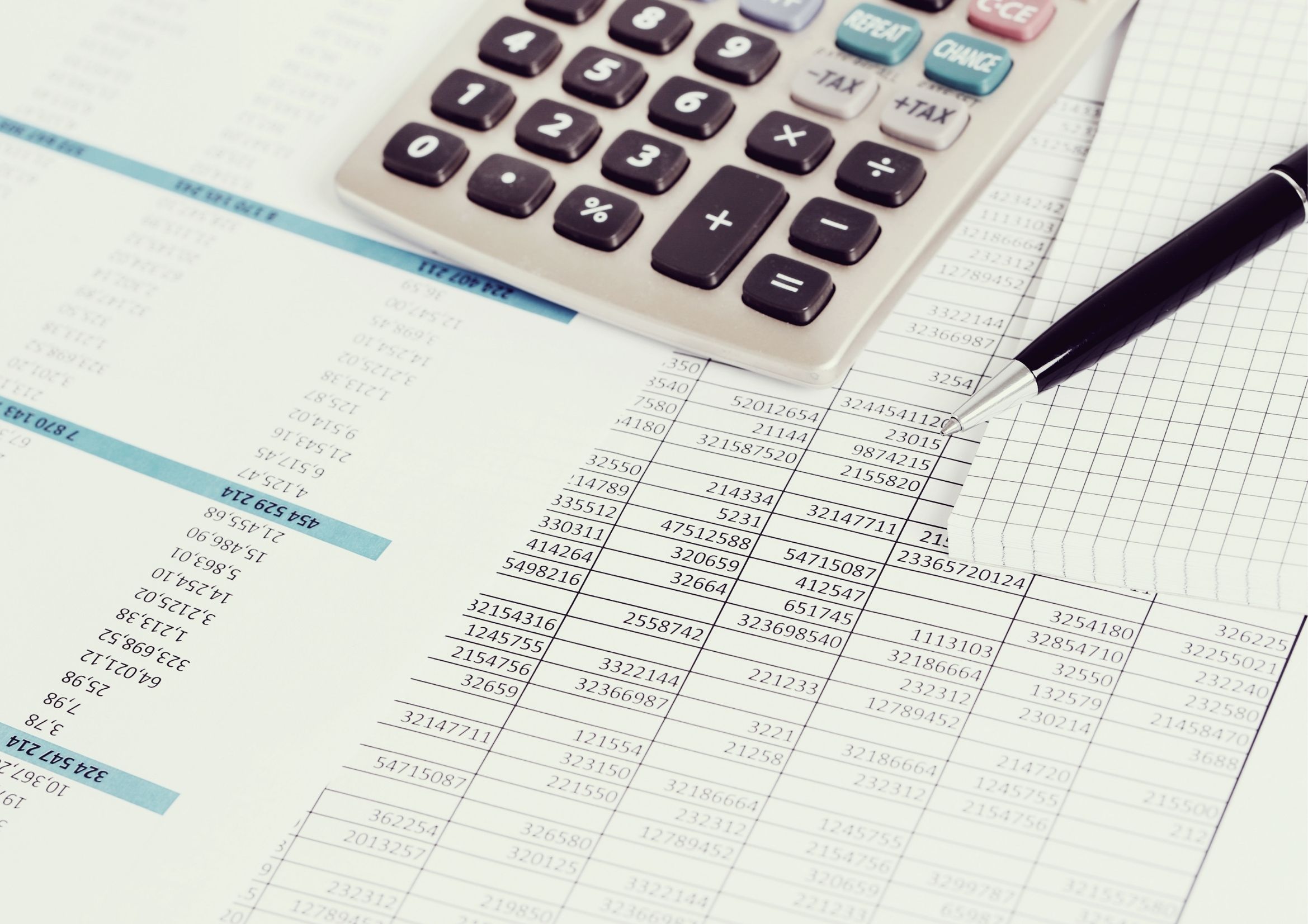 Calculadora e caneta sobre folhas com números, elementos relacionados à formação de preço