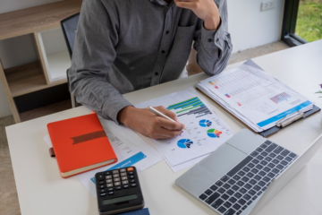 Pessoa fazendo análise, na mesa com gráficos, caderno, computador e calculadora, para ilustrar o processo de precificação inteligente